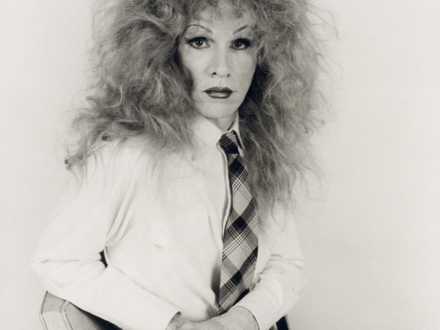 This image shows a person sitting in a chair who wears a very frizzy wig.