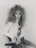 This black and white photograph shows a man wearing a frizzy wig while sitting in a chair.