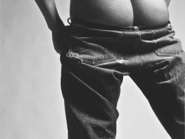 This black and white photograph shows a man seen from behind with his pants pulled down his legs.