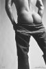 This black and white photograph shows a man seen from behind with his pants pulled down his legs.
