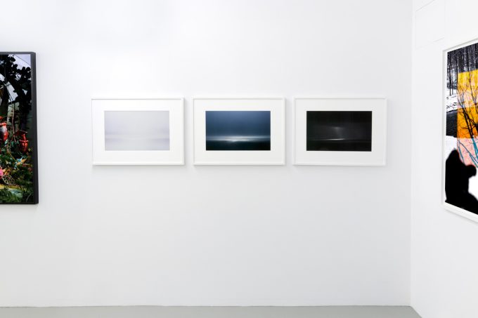 This photograph shows three color photographs of the horizon framed on the walls of a gallery.