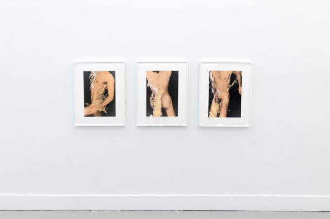 This photograph shows the walls of a gallery with hand painted silver gelatin prints of men floating underwater against floating colorful fabrics.