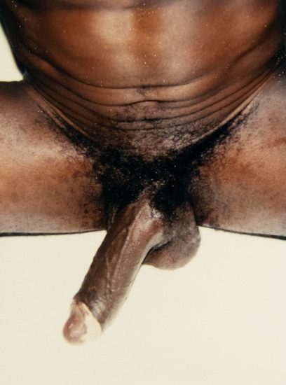 A color photograph of a nude man spreading his legs as seen from the front.