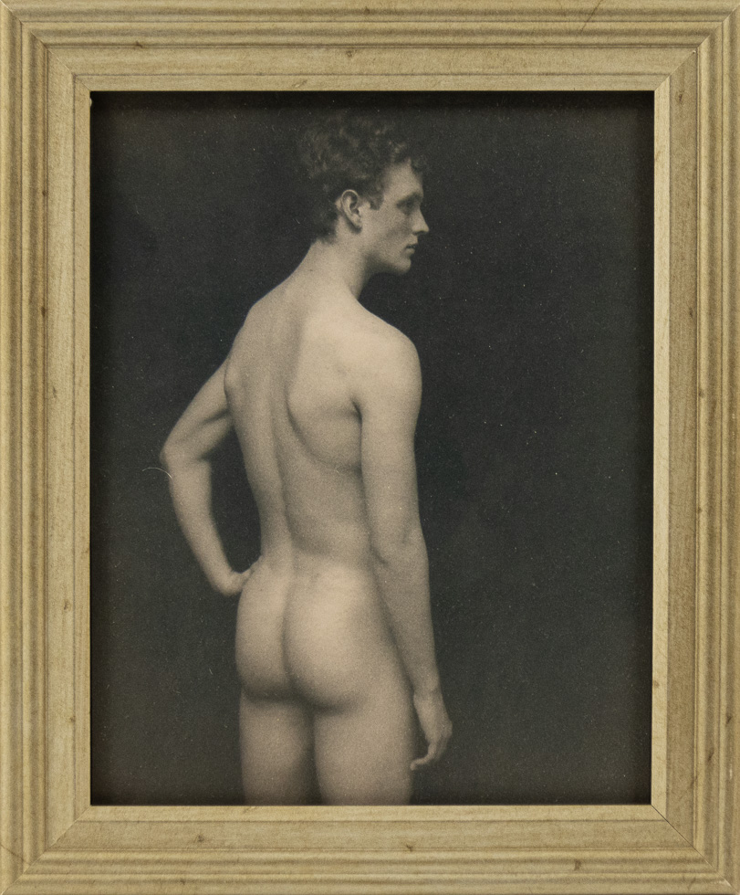 This framed photograph shows a naked man looking away from the camera with his hand on his hip.