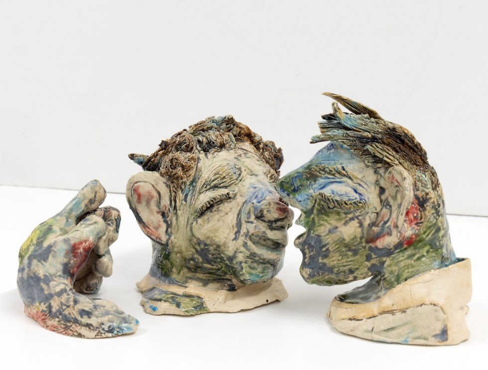 This image shows a green ceramic sculpture depicting two men's heads.