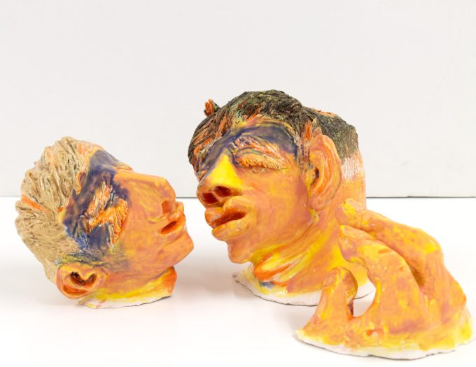 This image shows a bright orange ceramic sculpture of two people's heads.