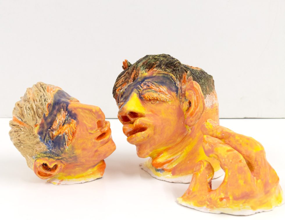 This image shows a bright orange ceramic sculpture of two people's heads.
