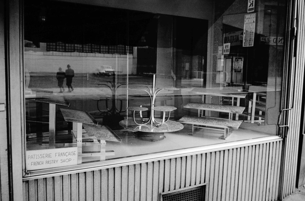 This black and white photograph shows an empty case in a bakery behind a glass window.