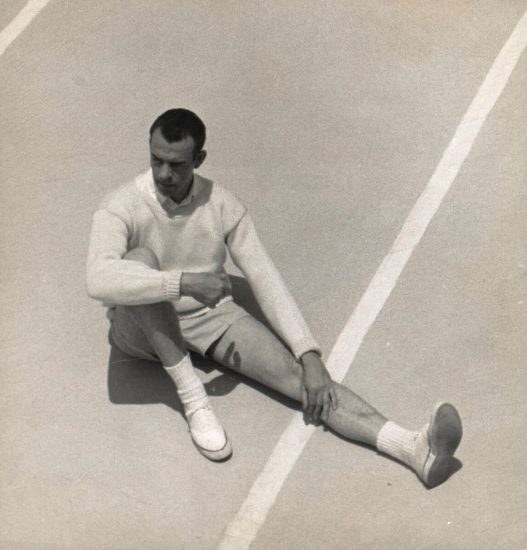 This black and white photograph shows a man in shirts sitting on a court. He is seen from above.