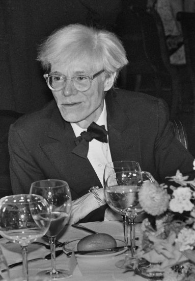 A black and white photograph of Andy Warhol at an event.